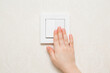 Little child hand pressing white plastic light switch buttons at wall in room. Turn on or turn off lighting. Closeup. Energy saving at home. Front view.