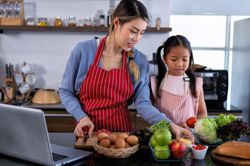 Wall Mural - Young mother teach daughter in the kitchen learn online cooking clean food from the laptop computer