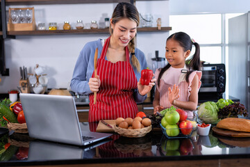 Wall Mural - Young mother teach daughter in the kitchen learn online cooking clean food from the laptop computer