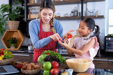 Wall Mural - Young mother teach daughter in the kitchen learn online cooking clean food from the laptop computer