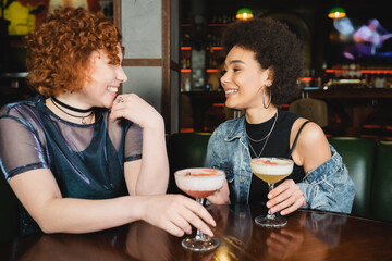 Wall Mural - Young multiethnic girlfriends talking near foam cocktails in bar.