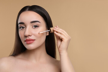 Canvas Print - Young woman applying essential oil onto face on beige background, space for text