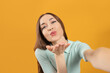 © New Africa - Beautiful young woman blowing kiss while taking selfie on yellow background