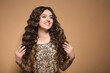 © New Africa - Beautiful young woman with long curly brown hair in golden sequin dress on beige background