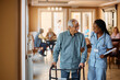 Happy black nurse assists senior man in using mobility walker at nursing home.