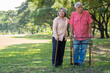 © Prot - An old elderly Asian man uses a walker and walks in the park with his wife.  Concept of happy retirement With Love and care from family and caregiver, Savings, and senior health insurance