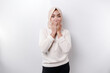 Portrait of a young Asian Muslim woman wearing a headscarf is tell be quiet, shushing with serious face, hush with finger pressed to lips, isolated by white background