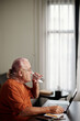 © DragonImages - Senior man drinking glass of water after fishing working on laptop