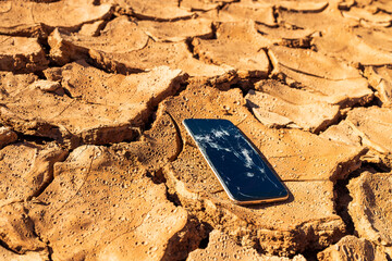 Canvas Print - smartphone with a broken screen on the soil during a drought