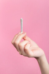 A woman's hand holds a joint with medical marijuana with her fingers.  On a pink background