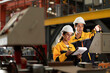 © Montri - Two professional engineer,worker,technician use clipboard discuss work, walk in steel metal manufacture factory plant industry. Black African American man and woman wear hard hat check quality machine