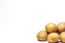 A Close Up Photograph Of A Pile Of Yellow And Brown Russet Potatoes In Lower Right Corner With White Background And Copy Space.