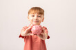 © Irina Mikhailichenko - Smiling child boy holding pink piggy bank. Money Saving Concept. saving money for future, insurance and investment concept. The child manages and deposits his finances.