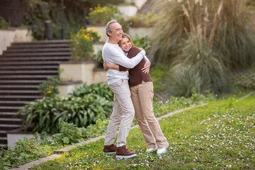 Wall Mural - Mature Spouses Embracing Standing In Green Park Outside, Looking Aside