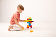 © Irina Mikhailichenko - A happy child collects a tower of colored cubes. The preschooler sits down at the white background and assembles the construction set. The boy smiles, pleased with the result.