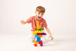 © Irina Mikhailichenko - A happy child collects a tower of colored cubes. The preschooler sits down at the white background and assembles the construction set. The boy smiles, pleased with the result.