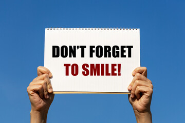 don't forget to smile text on notebook paper held by 2 hands with isolated blue sky background. this