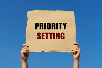 Priority setting text on box paper held by 2 hands with isolated blue sky background. This message board can be used as business concept about priority.