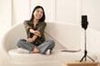 © Prostock-studio - Cheery pretty chinese lady recording video on smartphone, home interior