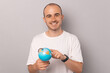 Wide smiling young bald man is looking and pointing at the Earth globe.