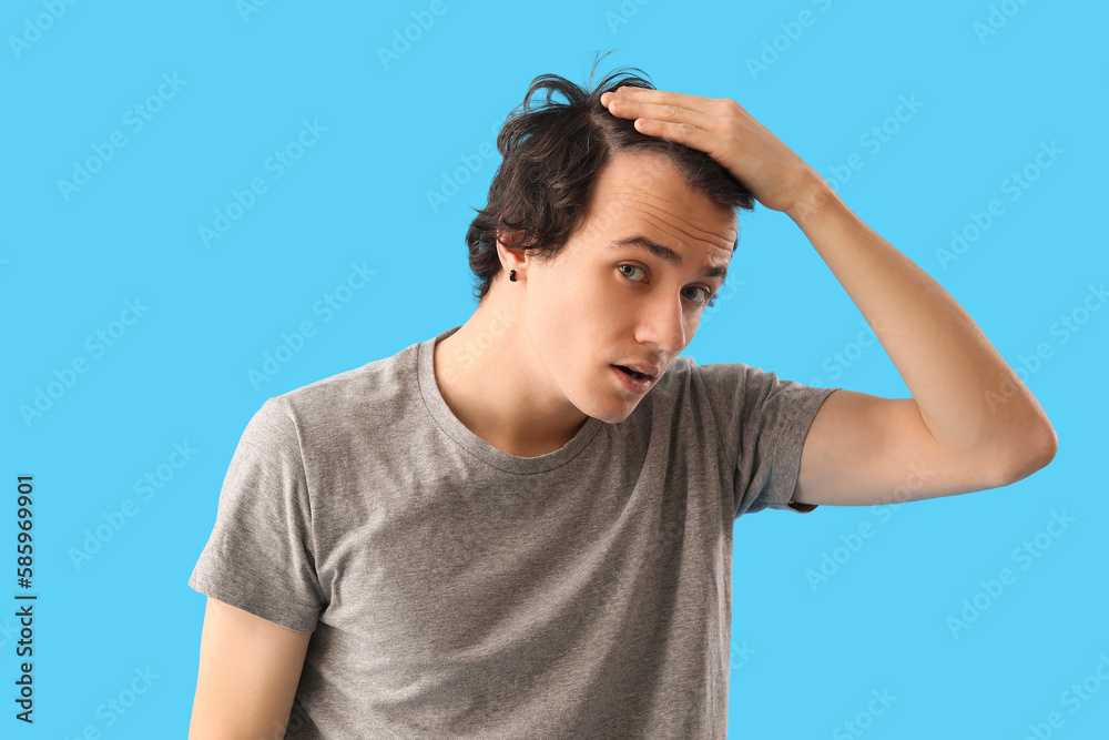 Young man with hair loss problem on blue background