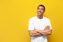 Young Pensive Afro American Guy In White Oversized T-shirt Stands On Yellow Isolated Background And Looks To The Side