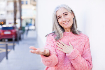 Wall Mural - senior retired pretty white hair woman feeling happy and in love, smiling with one hand next to heart and the other stretched up front