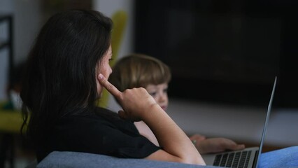 Wall Mural - Mother parenting with child in front of laptop screen working from home. Parent sitting on couch with toddler boy looking at computer