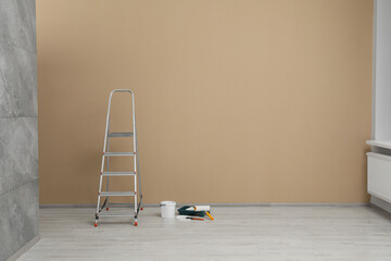 Poster - Metallic folding ladder and painting tools near beige wall indoors, space for text