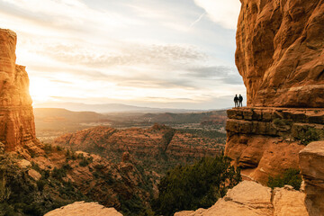 Wall Mural - Young heterosexual couple holds hands at viewpoint during dramatic sunset from Cathedral Rock in Sedona.