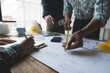 © Phimwilai - A group of engineers and architects are brainstorming, analyzing and taking notes using tape measure to measure house plans. Draft the house structure to establish the correct standards.