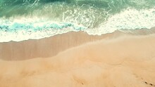 Aerial View Looking Straight Down Onto Crashing Waves Hitting A Golden Beach While Panning To The Right 