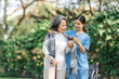 © NanSan - Young asian care helper with asia elderly woman on wheelchair relax together park outdoors to help and encourage and rest your mind with green nature. Wear a scarf over your shoulders with care.