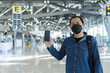 © Patcharanan - Asian man passenger wearing protective face mask showing e-ticket to flight. Touris man showing boarding pass on mobile phone. Young male showing smartphone at airport. Travel concept.