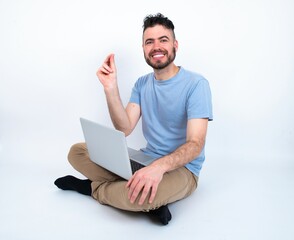 Sticker - Young caucasian man with laptop sitting over white studio pointing up with hand showing up seven fingers gesture in Chinese sign language QÄ«.