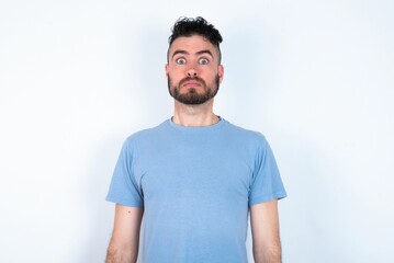 Wall Mural - Stunned Young caucasian man wearing blue T-shirt over white background stares reacts on shocking news. Astonished man holds breath