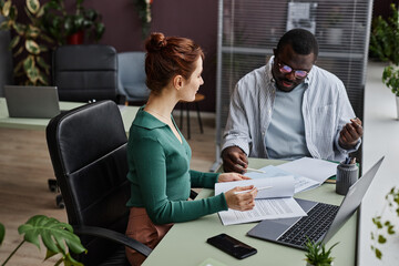 High angle view at two people discussing project and reading documents at workplace in office decorated with plants