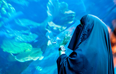 Arab woman at aquarium in Dubai with fish close up. Underwater wildlife