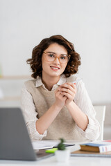 Wall Mural - cheerful student in glasses smiling near laptop and dictionary while learning foreign language at ho