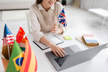 Wall Mural - cropped view of smiling language teacher with flag of united kingdom using laptop during online less