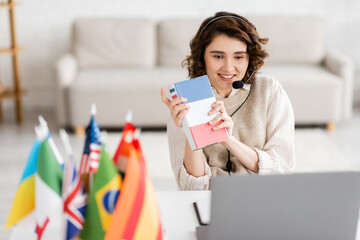 Wall Mural - smiling language teacher in headset showing french textbook during video lesson on laptop near blurr