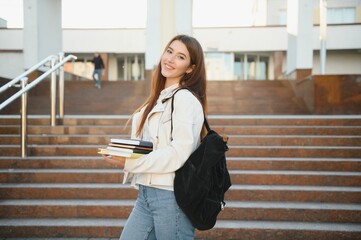 Wall Mural - Cheerful attractive young woman with backpack and notebooks standing and smiling.