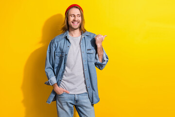 Poster - Photo of friendly guy with long hairdo dressed jeans shirt look directing empty space hand in pocket isolated on yellow color background