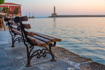 Wall Mural - Sunrise view of Venetian lighthouse and a bench at the port of Chania at Crete, Greece