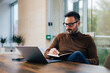 © bnenin - Focused businessman looking at the laptop, taking notes in notebook, sitting at the office.