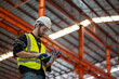 Low angle view of a worker wearing reflective jacket holding digital tablet standing in factory warehouse