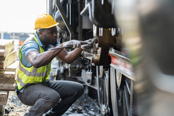 Male engineer maintenance locomotive engine, wearing safety uniform, helmet and gloves in locomotive repair garage. Male railway engineer use wrench repair train wheel in train garage