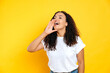 © Kateryna - Photo of positive excited stylish brazilian or hispanic curly haired woman, holding palm near open mouth, calling someone, yelling announcement, stand on isolated yellow background