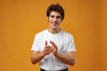 Portrait of cheerful young man clapping hands on yellow background.