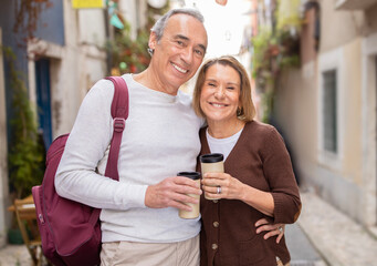 Wall Mural - Happy Mature Spouses Embracing Holding Coffee Cups Standing In Lisbon